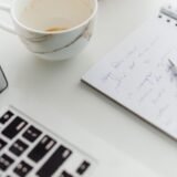 Persoană care redactează la laptop titlul unui comunicat de presă, cu notițe tipărite alături